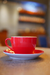 Bright red coffee cup on saucer in cozy cafe setting