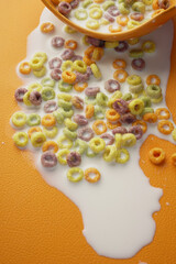 Colorful cereal spills milk on an orange surface in the kitchen