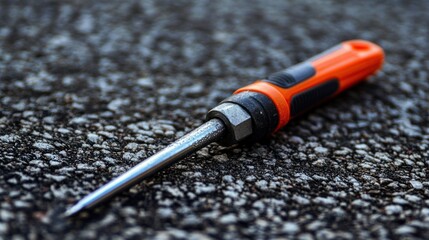 Orange and black screwdriver on asphalt