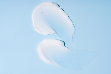 Texture of white cream on blue background. Smear of moisturizer close up. Lotion swatch. Beauty...