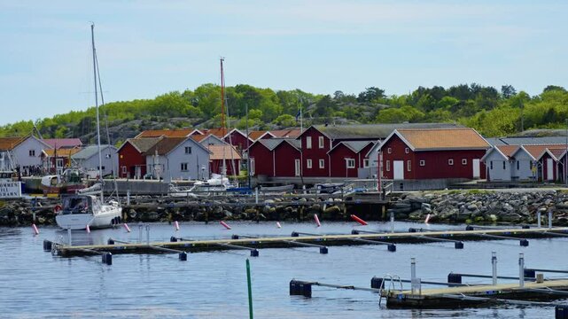 Push in shot of harbor with boats and red houses during the day in Koster Islands, Bohuslan, Sweden, establishing shot