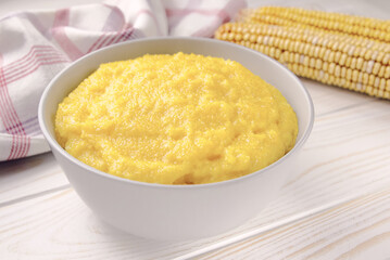 Delicious corn porridge in a bowl on a white wooden table.
