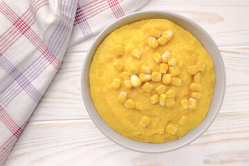 Delicious corn porridge in a bowl on a white wooden table.