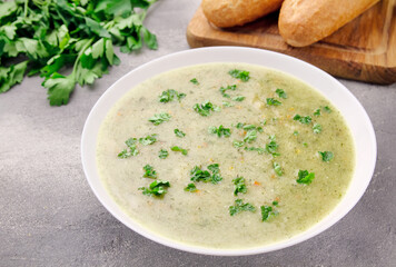 Homemade cream soup with chicken and herbs in a white plate on a gray background.