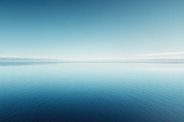 Obraz premium Serene landscape of calm blue water meeting a hazy mountain range under a clear sky.
