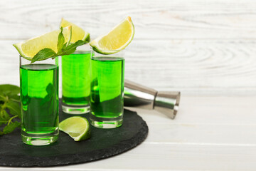 Sweet refreshing mint liqueur, with ice and mint leaves on table background, Shots with lime slice and mint flat lay