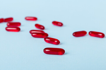 Heap of red pills on colored background. Tablets scattered on a table. Pile of red soft gelatin...