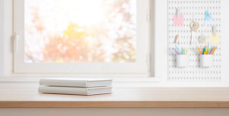 White books on table and copy space in blurred study room with window sill and stationery as background
