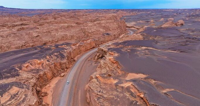 Aerial view of a winding road through the spectacular yardang landform canyon and vast desert landscape in Xinjiang, China.
