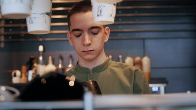 Closeup of a young barista's face as he carefully wipes cups with a cloth during the morning opening hours of a modern coffee shop - Powered by Adobe