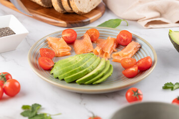 Plate with smoked salmon, avocado and cherry tomatoes on a light background. Fresh and healthy ingredients. Balanced diet concept