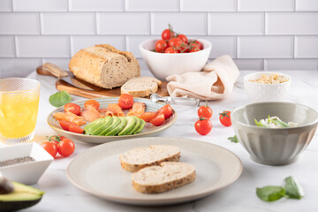 Table with ingredients for healthy toasts: whole grain bread, avocado, cherry tomatoes, nuts, cottage cheese bowl, and orange kombucha glass. Concept of healthy breakfast and balanced food