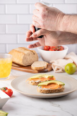 Male Hands Seasoning Multigrain Toast with Pepper. Bright Healthy Kitchen. .Sunlit marble surfaces and fresh herbs. Perfect for spice brands or farm-to-table concepts