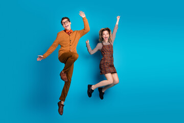 Happy young couple in stylish retro outfits jumping joyfully against a vibrant blue background