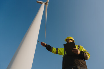 Engineers in safety gear conduct a detailed inspection of wind turbine blades at a construction site. Large blades are placed on the ground, highlighting the renewable energy technology.