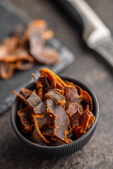 Beef jerky. Dried spiced meat in bowl on black table.