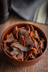 Beef jerky. Dried spiced meat in bowl on wooden table.