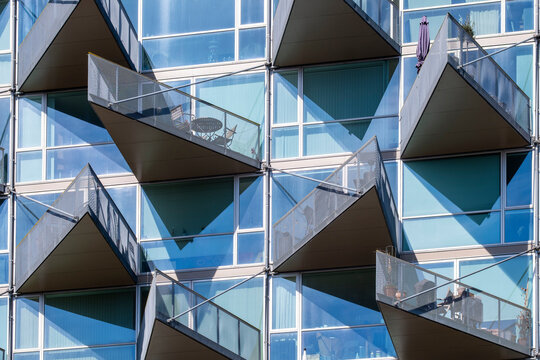 Geometric glass balconies on a modern residential facade in Copenhagen with sharp angles and clear reflections, ideal for commercial and architectural stock use, daylight scene.