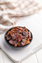 Beef jerky. Dried spiced meat in bowl on white table.