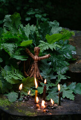 witch doll and burning candles in forest, natural dark background. Forest grandmother, defender...