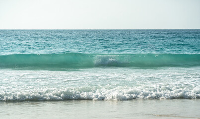 Clear turquoise waves gently crashing on a peaceful sandy beach at a tropical island coastline