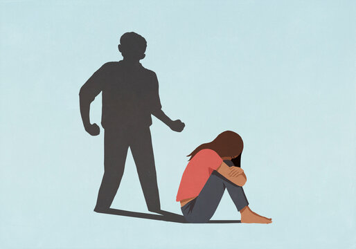 Aggressive male shadow looming over scared woman hugging knees against blue background
