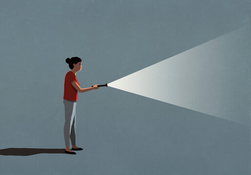 Woman holding bright flashlight in darkness

