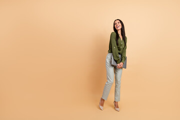 Fototapeta premium Elegant professional woman in green top holding a tablet, posing confidently against a beige background