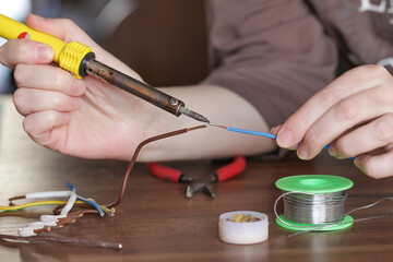 Woman Solders cooper wires with a soldering iron. Soldering, maintenance and repair work at home