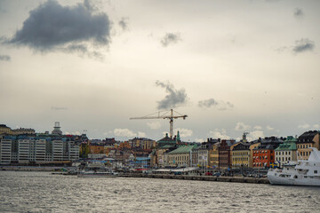 Fototapeta premium Wide angle view of Scandinavian colorful houses next to the seaside with a crane and grey cloudy autumn sky in the background, Stockholm, Sweden
