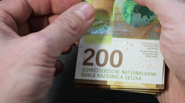 Closeup of male hand counting 200 Swiss francs