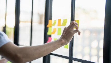 Man organizing project tasks Colorful sticky notes on glass of meeting room