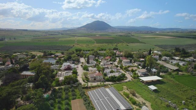 Mount Tabor creates a dramatic backdrop to this overhead shot of Kfar Kish - Israel, peaceful coexistence of village architecture with surrounding farmlands on a summer day in northern contry