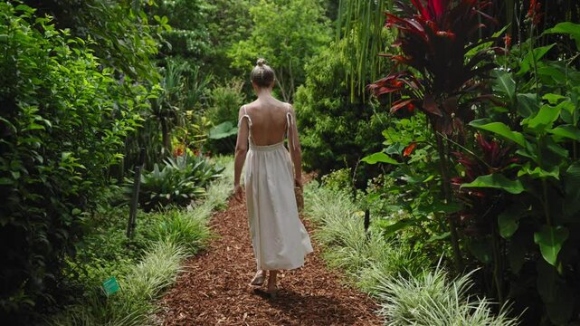 A young, beautiful tourist woman walks through Sydney's Royal Botanic Garden on a bright summer day. Lush greenery, exotic flowers and tropical plants surround her in this vibrant nature setting.