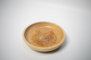 A round wooden plate with a smooth finish, placed on a white surface.