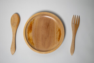 A wooden spoon, plate, and fork set on a white background, arranged neatly for a natural dining setup.