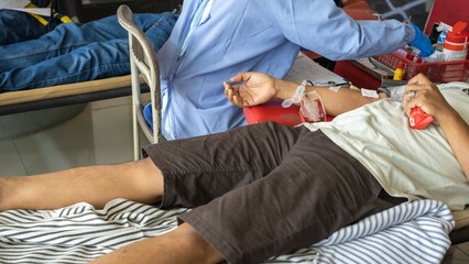 Fototapeta premium Close-up of a man donating blood during a healthcare event, showing a needle in his arm and a medical worker assisting in the background.