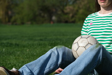 Naklejka premium Unrecognizable person in a striped sweater kneels on green grass, hands resting on knees with grass stains. Concept of daily stains on clothes