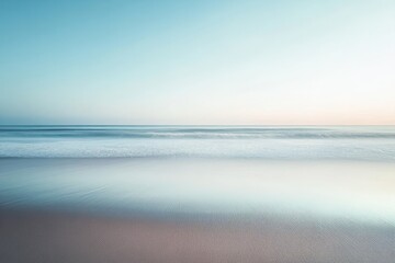 Obraz premium Gentle ocean waves meet a pale sandy shore at sunrise.