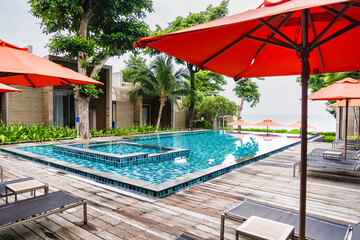 Rayong, Thailand - April, 03, 2025 :Luxurious outdoor swimming pool with red umbrellas and sun...