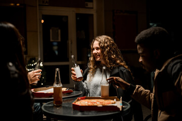 Friends enjoying pizza and drinks at a cozy outdoor gathering on a chilly evening
