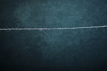 A single, frayed piece of string stretches across a dark, textured surface.