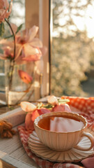 Vintage teacup with tea on a wooden tray by a window, surrounded by pink flowers and soft sunlight, with a warm and peaceful morning atmosphere