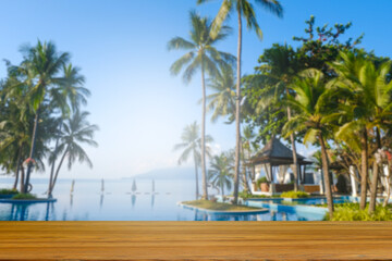 Obraz premium Wood floor counter top There is a view of the swimming pool and sea in the background of the resort. A blurry garden of trees is visible. of decorative design ideas