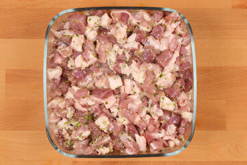 Diced and seasoned pork meat, prepared with spices for sausage making, fills a square glass dish on a wooden surface