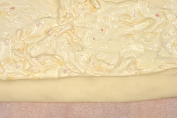 A sheet of puff pastry covered with a mixture of sour cream and grated cheese is being rolled up on parchment paper