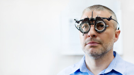 Middle aged man undergoing detailed vision test while using phoropter in clinical setting for eye examination, closeup shot
