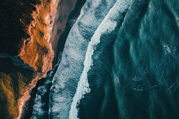 Naklejka premium Aerial view of crashing waves meeting a rugged coastline.