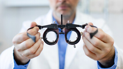 Professional male optometrist at work, holding an optometer, with an eye check chart in the...