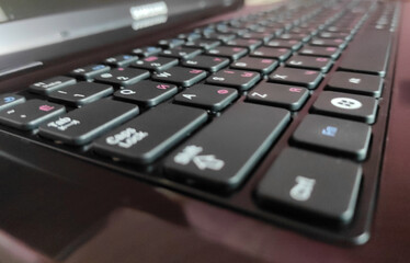 A close-up, angled view of a black laptop keyboard, focusing on the keys with white and pink...